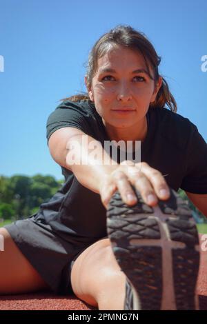 Nahaufnahme einer jungen lateinamerikanischen argentinierin in schwarzer Sportbekleidung, konzentriert sich auf dem Boden, mit der Hand auf der Fußspitze, senkrecht Stockfoto