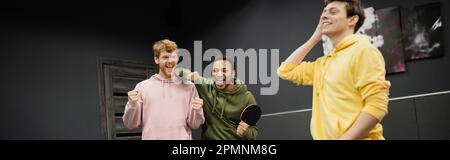 Fröhliche Männer mit Tennisschläger, die in der Nähe eines Freundes im Spielclub eine Geste zeigen, Banner, Stock Image Stockfoto