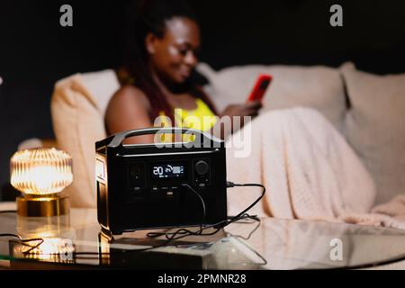 Frau sitzt mit Batterie-Energiebank, die Beleuchtung und Notversorgung bereitstellt, wenn der Strom ausfällt. Stockfoto