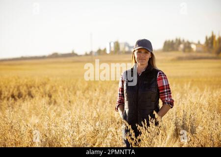 Porträt einer Reifen Farmfrau, die in einem Getreidefeld steht und während der Ernte bei Sonnenuntergang für die Kamera posiert; Alcomdale, Alberta, Kanada Stockfoto