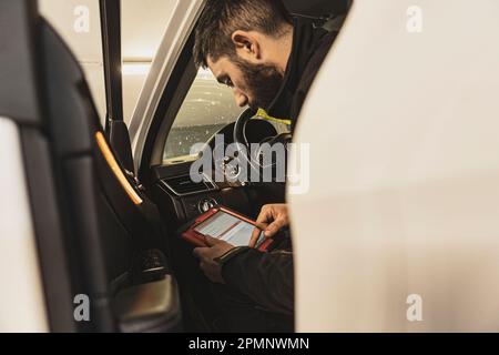 Mailand, Italien 11. april 2023: Die Hände eines Mechanikers verwenden ein Diagnosegerät, um Fehler am Computersystem eines modernen Autos in einer Garage zu beheben. Stockfoto