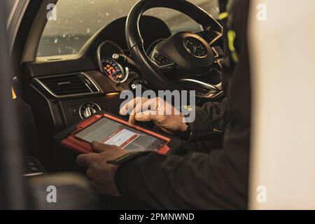 Mailand, Italien 11. april 2023: Die Hände eines Mechanikers verwenden ein Diagnosegerät, um Fehler am Computersystem eines modernen Autos in einer Garage zu beheben. Stockfoto
