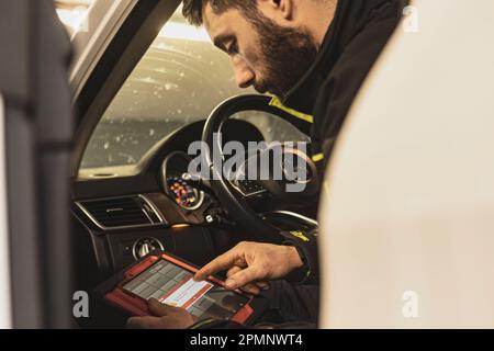 Mailand, Italien 11. april 2023: Die Hände eines Mechanikers verwenden ein Diagnosegerät, um Fehler am Computersystem eines modernen Autos in einer Garage zu beheben. Stockfoto