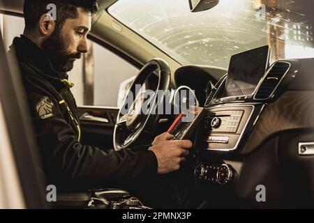 Mailand, Italien 11. april 2023: Die Hände eines Mechanikers verwenden ein Diagnosegerät, um Fehler am Computersystem eines modernen Autos in einer Garage zu beheben. Stockfoto