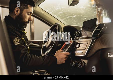 Mailand, Italien 11. april 2023: Die Hände eines Mechanikers verwenden ein Diagnosegerät, um Fehler am Computersystem eines modernen Autos in einer Garage zu beheben. Stockfoto