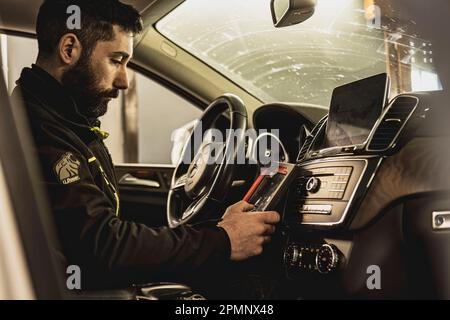 Mailand, Italien 11. april 2023: Die Hände eines Mechanikers verwenden ein Diagnosegerät, um Fehler am Computersystem eines modernen Autos in einer Garage zu beheben. Stockfoto