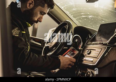 Mailand, Italien 11. april 2023: Die Hände eines Mechanikers verwenden ein Diagnosegerät, um Fehler am Computersystem eines modernen Autos in einer Garage zu beheben. Stockfoto
