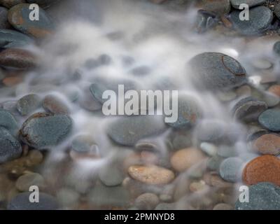 Verschwommenes Meerwasser fließt über Kieselsteine am Strand; Greymouth, Südinsel, Neuseeland Stockfoto