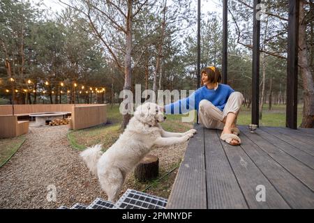 Eine Frau mit Hund ruht in der Nähe einer hölzernen Hütte in der Natur Stockfoto