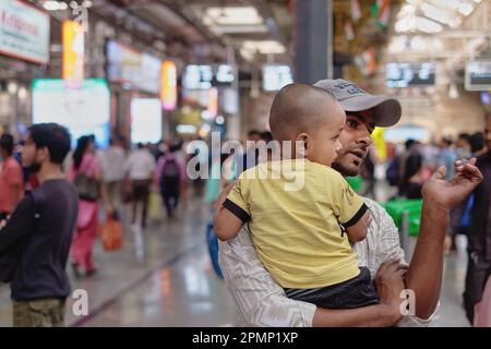 Ein junger indischer Vater, der seinen kleinen Sohn trug, während er auf einen Vorortzug am Chhatrapati Shivaji Maharaj Terminus (CSMT) in Mumbai, Indien wartete Stockfoto