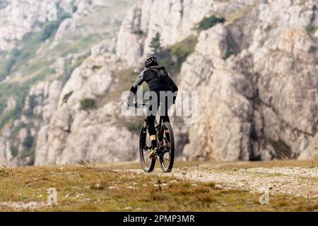 Männlicher Radfahrer fährt Mountainbike in der Bergregion und reist Rad. Rucksack auf der Rückseite des Mountainbikers Stockfoto