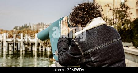 Ein junger Mann steht auf dem Pier und blickt durch ein Teleskop, mit dem riesigen Ozean im Hintergrund. Stockfoto