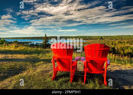 Zwei große rote Stühle mit warmem Licht bei Sonnenuntergang auf einem Feld mit Blick auf ein Flusstal mit dramatischen Wolken und blauem Himmel; Calgary, Alberta, Kanada Stockfoto