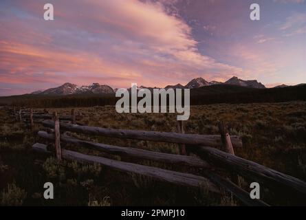 Die Sawtooth Range, ein Teil der Rocky Mountains, ist eine Kulisse für einen Split-Rail-Zaun bei Sonnenuntergang; Idaho, Vereinigte Staaten von Amerika Stockfoto