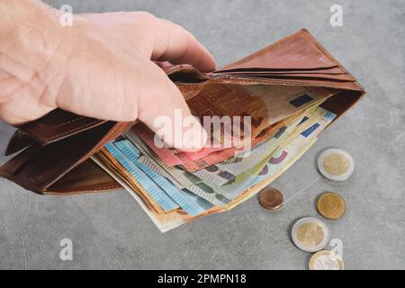 Ein älterer Mann hält eine Geldbörse mit Euro-Banknoten in der Hand, Euro-Banknoten in der Geldbörse. Geldbörse mit Geld in der Hand eines Mannes, Hintergrundidee von Bezahlen Stockfoto