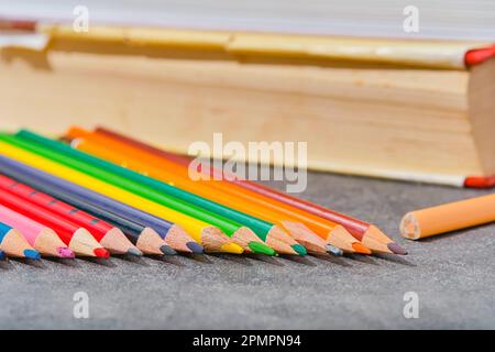Farbige Bleistifte und alte Bücher auf einem hellgrauen Tisch, Nahaufnahme, selektiver Fokus, verschwommener Hintergrund. Schulanfang, Bildungskonzept, Layoutvorlage Stockfoto