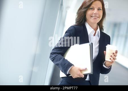 Fröhliche Geschäftsfrau, die Ordner in der Hand hält und Kaffee trinkt. Eine weibliche Geschäftsfrau, die Akten trägt und Tee trinkt, während einer Pause in einem Stockfoto