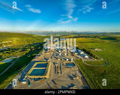 Luftaufnahme einer Gasanlage entlang eines Flusses mit blauem Himmel und Wolken und Bergen im Hintergrund, westlich von Cochrane, Alberta, Kanada Stockfoto