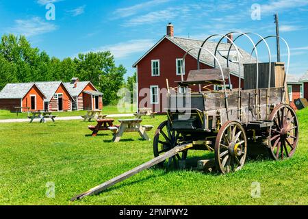 Alter Holzwagen mit rot bemalten Gebäuden, Picknicktischen, blauem Himmel und Wolken im Hintergrund, südlich von Longview, Alberta, Kanada Stockfoto