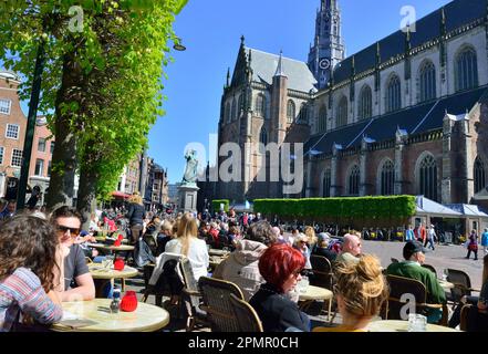 Menschen genießen die Frühlingssonne in den Restaurants um den zentralen Marktplatz (Grote Markt) neben der gotischen Kirche Grote Kerk, Haarlem Stockfoto