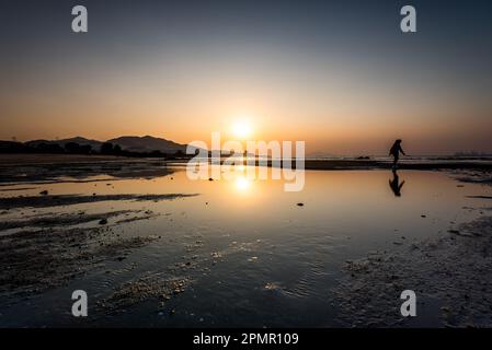 Eine Person, die bei Sonnenuntergang am See entlang in der Landschaft von Hongkong spaziert Stockfoto