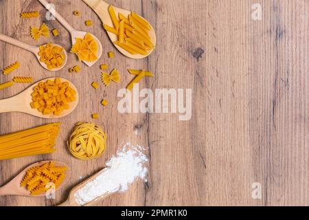 Verschiedene Nudelmischungen auf rustikalem Holzhintergrund, Sacktuch und Holzlöffel. Diät und Speisekonzept. Stockfoto
