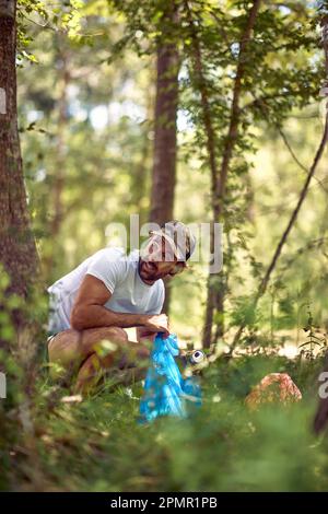 Junger Mann, der Müll im Freien aufsammelt. Naturreinigung, ehrenamtliche Ökologie grünes Konzept. Stockfoto