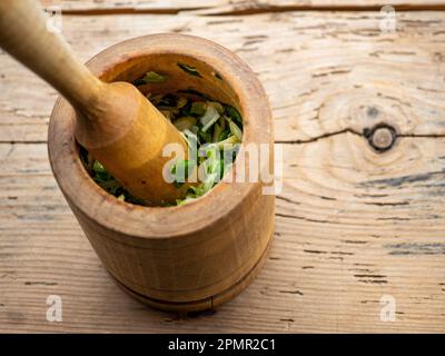 Knoblauch in einem Holzmörtel und Stößel auf einem Holztisch zerstoßen Stockfoto