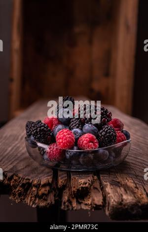 Verschiedene Beeren auf einer Glasplatte. Rote Beeren auf einem Holztisch. Schöne Zusammensetzung von Beeren. Vertikaler Rahmen. Stockfoto