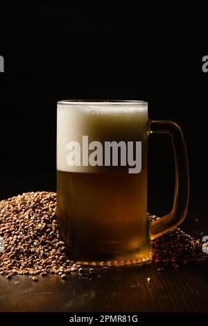 Biertasse mit frischem schaumhaltigem Bier auf dunklem Hintergrund. Das Glas ist in einem Haufen Malz. Stockfoto