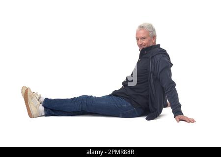 Seitenansicht eines Mannes, der mit gestreckten Beinen auf dem Boden sitzt und auf die Kamera auf weißem Hintergrund schaut Stockfoto