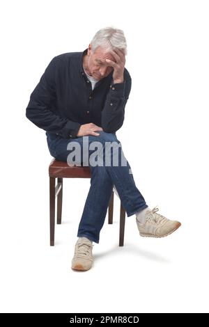 Trauriger Mann, der auf einem Stuhl auf weißem Hintergrund sitzt Stockfoto
