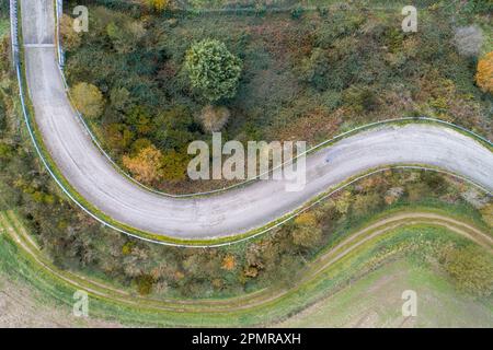 Dies ist ein Top-down-Blick auf eine herbstliche gewundene Straße, die von einem üppigen Wald umgeben ist Stockfoto