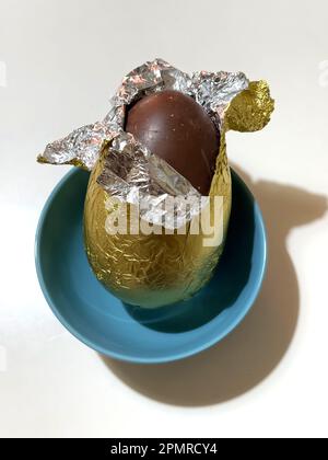 Ein Schokoladen-osterei, in Blechfolie verpackt, in einer türkisfarbenen Schüssel mit weißem Hintergrund Stockfoto