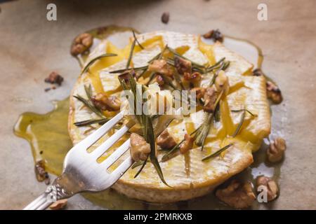 Ein Stück gebackener Camambert auf einer Gabel. Köstlicher gebackener Käse mit Honig, Walnüssen, Kräutern und Birnen Stockfoto