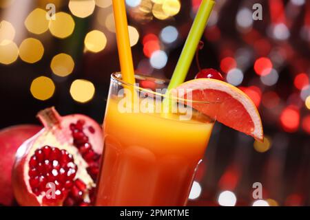 Ein Glas leckeren Tequila Sunrise und Granatapfel gegen verschwommenes Licht, Nahaufnahme Stockfoto