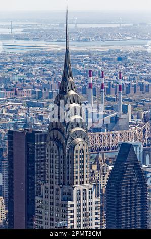 Blick von oben: Der Edelstahlspieß des New York City Icon Chrysler Building leuchtet unter der Mittagssonne; der Stadtteil Queens liegt dahinter. Stockfoto