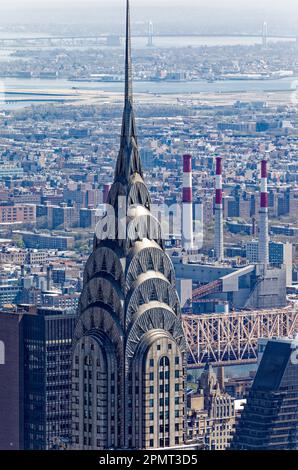 Blick von oben: Der Edelstahlspieß des New York City Icon Chrysler Building leuchtet unter der Mittagssonne; der Stadtteil Queens liegt dahinter. Stockfoto