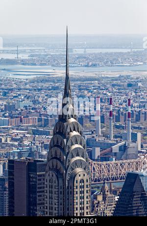 Blick von oben: Der Edelstahlspieß des New York City Icon Chrysler Building leuchtet unter der Mittagssonne; der Stadtteil Queens liegt dahinter. Stockfoto