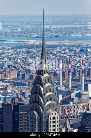 Blick von oben: Der Edelstahlspieß des New York City Icon Chrysler Building leuchtet unter der Mittagssonne; der Stadtteil Queens liegt dahinter. Stockfoto