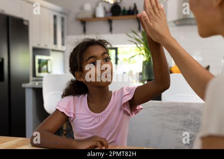 Rücksichtsvolle birassische Tochter, die mit ihrer Mutter an einem Tisch in der Küche sitzt Stockfoto