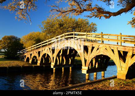 Eine kunstvoll verzierte Holzbrücke erstreckt sich über einen kleinen Bach in einem ruhigen öffentlichen Park Stockfoto