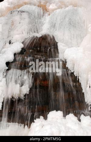 An einem kalten Wintertag fließt Wasser aus einem Wasserfall weiter, obwohl die Oberfläche gefroren ist Stockfoto