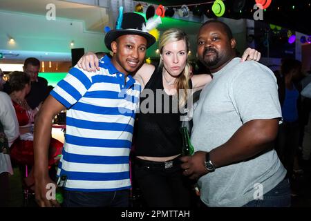 Drei junge Erwachsene, eine weiße Frau und zwei afroamerikanische Männer posieren zusammen in einem Nachtclub Stockfoto