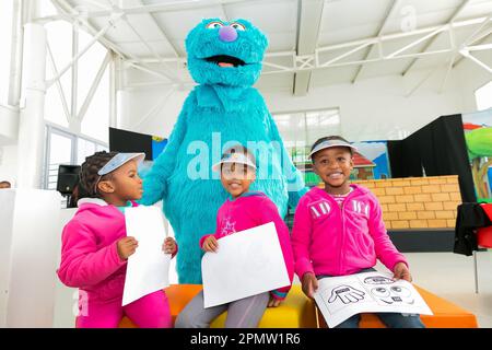 Drei kleine Kinder lächeln und posieren für die Kamera vor einem großen, weichen, blauen Teddybären Stockfoto