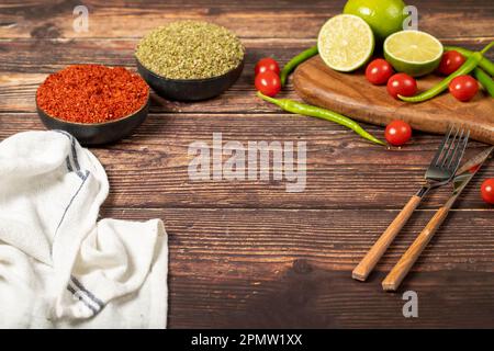 Leeres Schneidebrett aus Holz mit Kopierbereich, umgeben von Paprika, Kräutern, Tomaten, Zitrone und anderen köstlichen aromatisierten Gemüsesorten auf dem Tisch Stockfoto