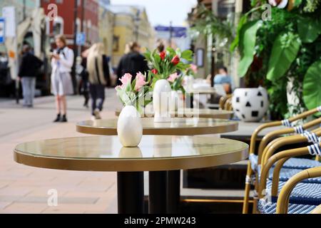 Straßencafe in der Stadt mit leeren Tischen draußen im Hintergrund für Spaziergänger. Blumen in Vasen auf runden Tischen an sonnigen Tagen Stockfoto