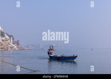 Varanasi, Uttar Pradesh, Indien - November 2022: Ein Blick auf die heiligen Ghats von Varanasi mit einem Bootsmann, der auf dem ganges segelt. Stockfoto