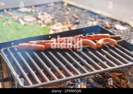 Grillen Sie im Freien mit frischen Würsten und brennenden Blättern an einem heißen Sommertag. Stockfoto