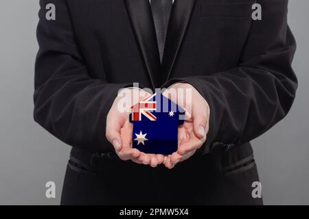 Australische Person, die ein Holzhaus hält, mit der Flagge Australiens Finanzen, Investitions-, Hypotheken-, Kredit- und Kreditkonzept Stockfoto